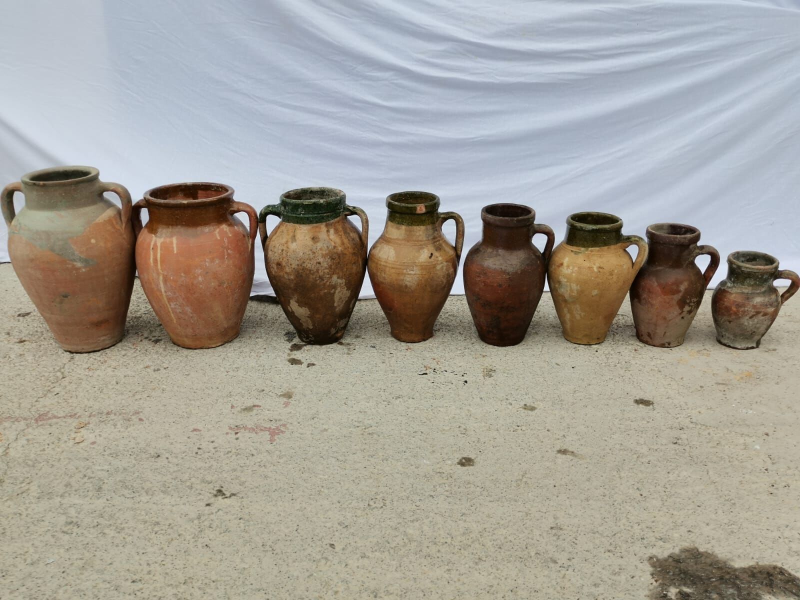 Konya Green Amphora, Small — row of small brown and terracotta jars on pale ground
