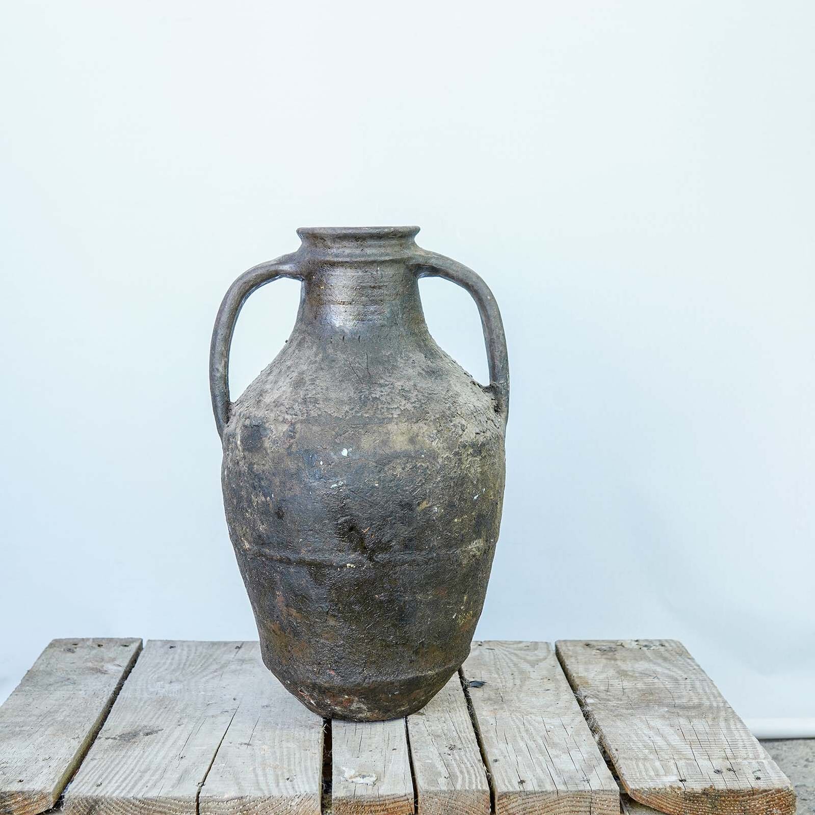 Tall Oil Amphora — tall dark clay amphora with two handles on a wooden pallet