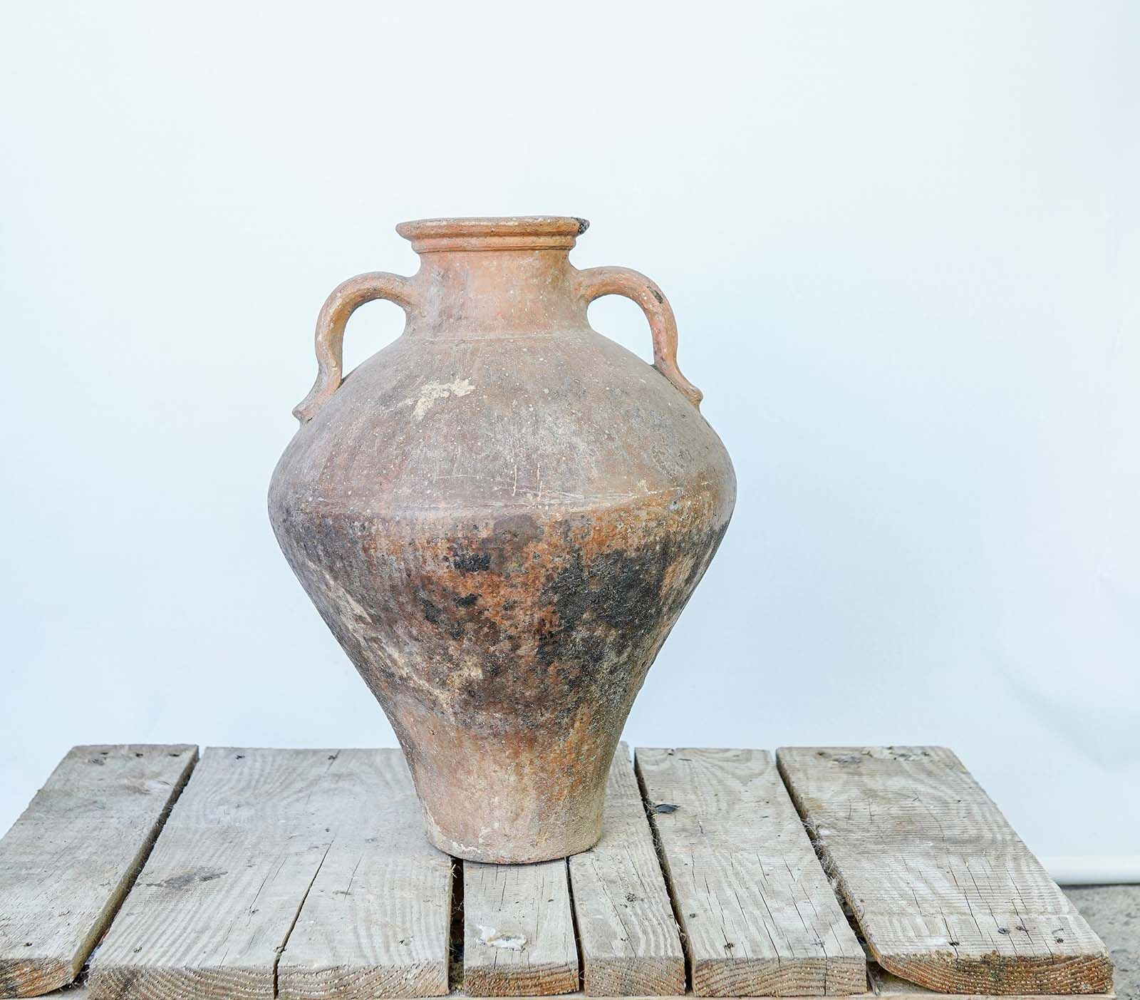 Tall Oil Amphora — rose-toned clay amphora with two handles on a wooden pallet