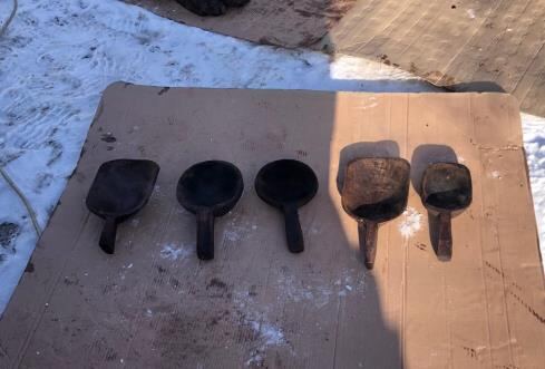 Five dark wooden scoops with short handles lined up on a cardboard sheet