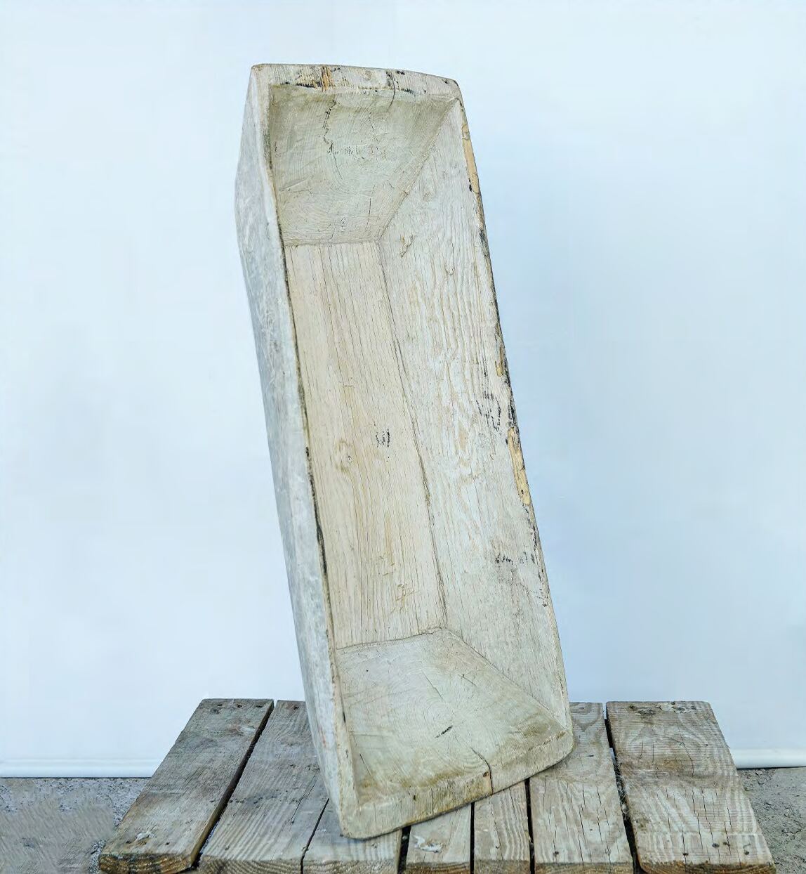 Long narrow wooden trough in pale weathered timber standing on a plank floor