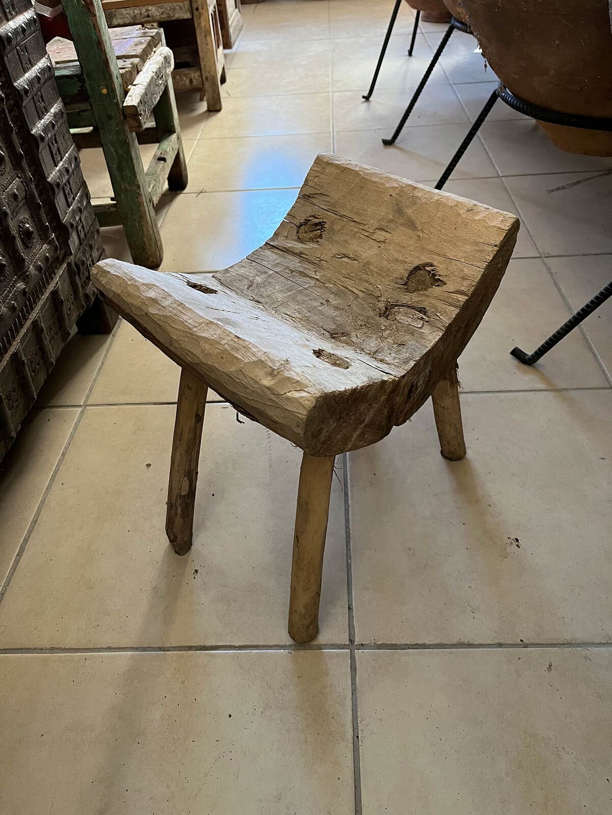 Hand-Hewn Wooden Stool — curved-seat wooden stool with splayed legs on a tiled floor