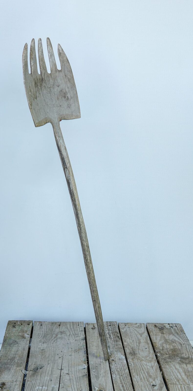 Wooden Pitchfork — tall wooden pitchfork with a long handle leaning on a pallet