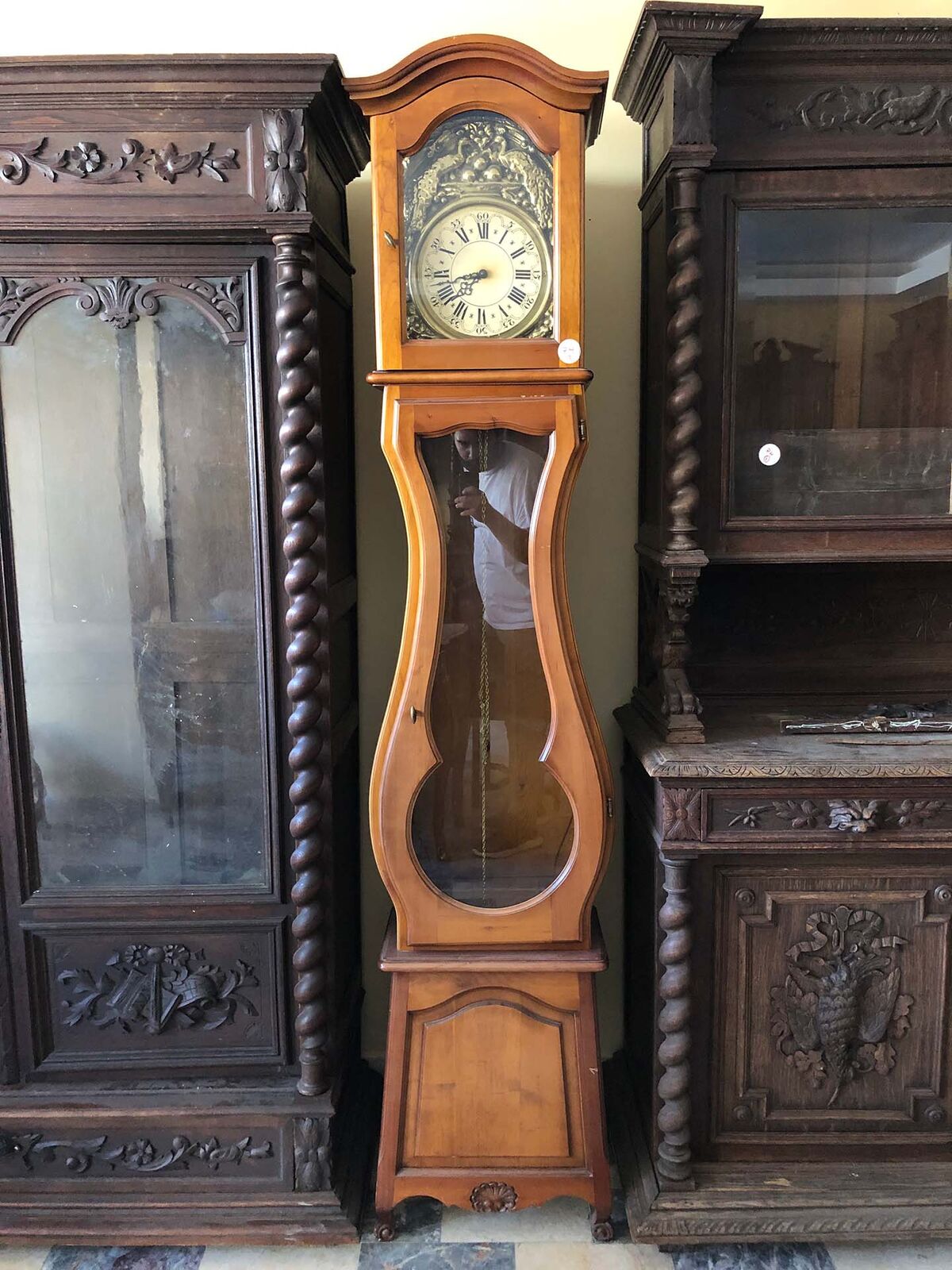 Longcase Clock — tall honey-coloured wooden longcase clock with a painted dial and a glass pendulum window