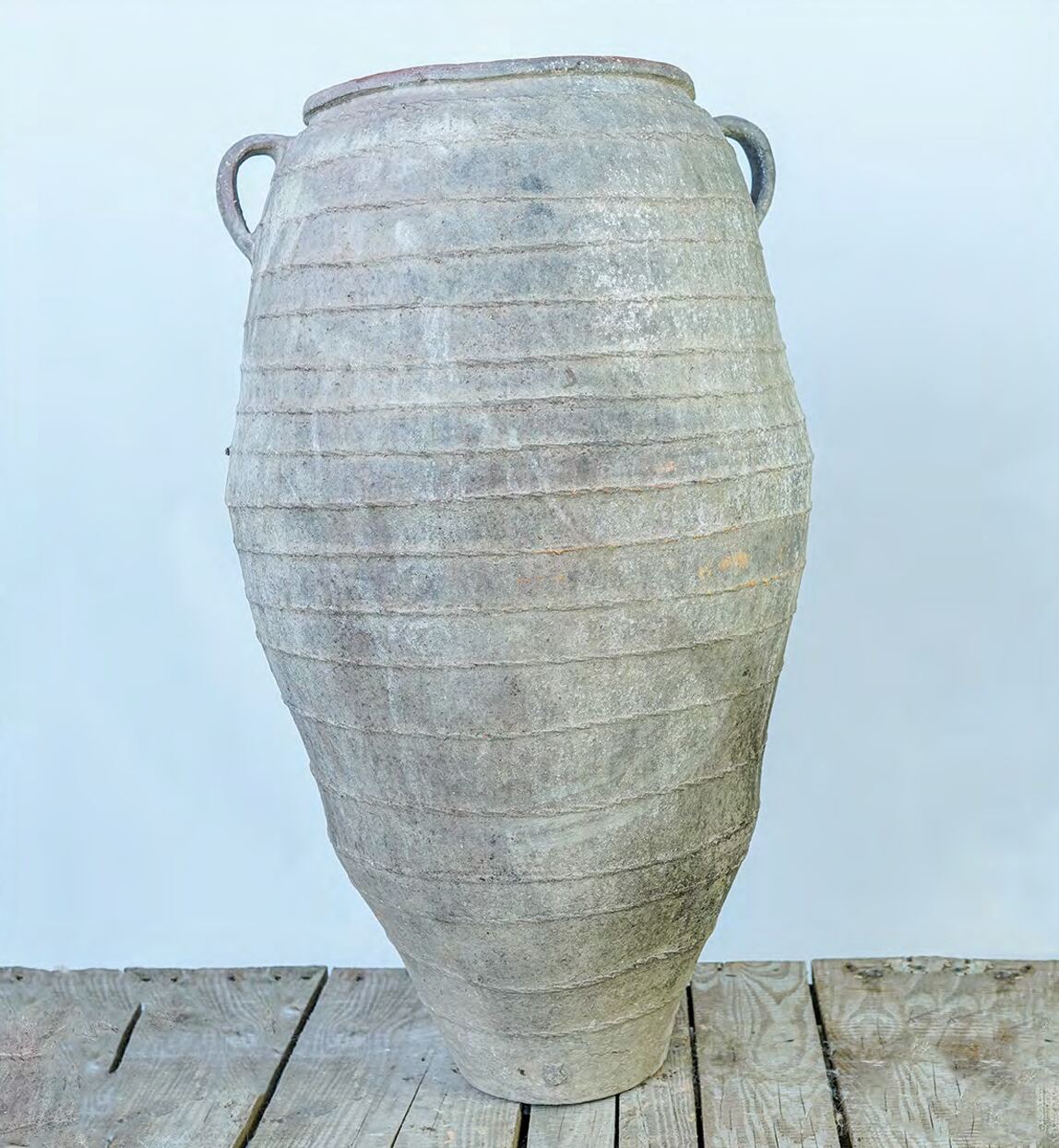 Tall grey two-handled jar with a grooved ovoid body standing on a plank floor