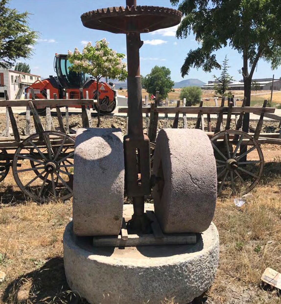 Two stone millstones on a round stone base with an iron mast and gear, outdoors
