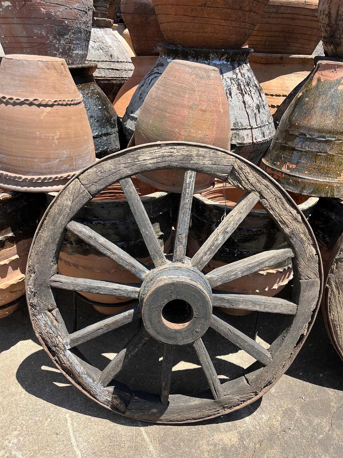 Antique Cart Wheel — old wooden cart wheel with iron hub among clay pots