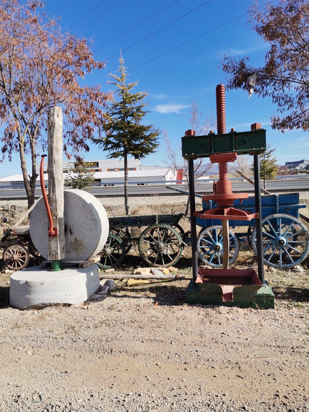 Red Iron Screw Press — iron press beside a round stone wheel in a yard
