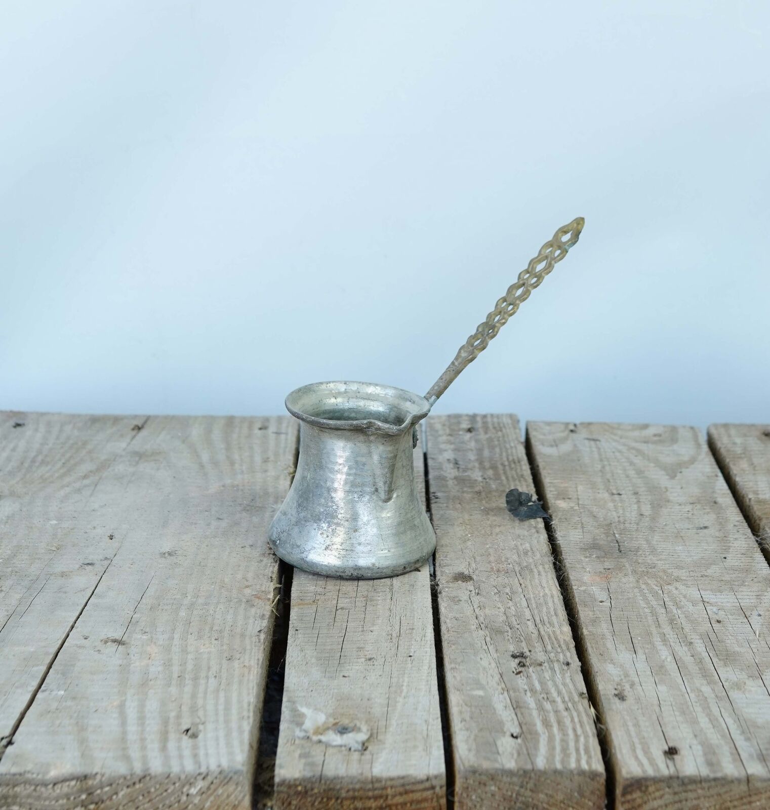 Long-Handled Coffee Pot — metal coffee pot with a long curved handle on a wooden pallet